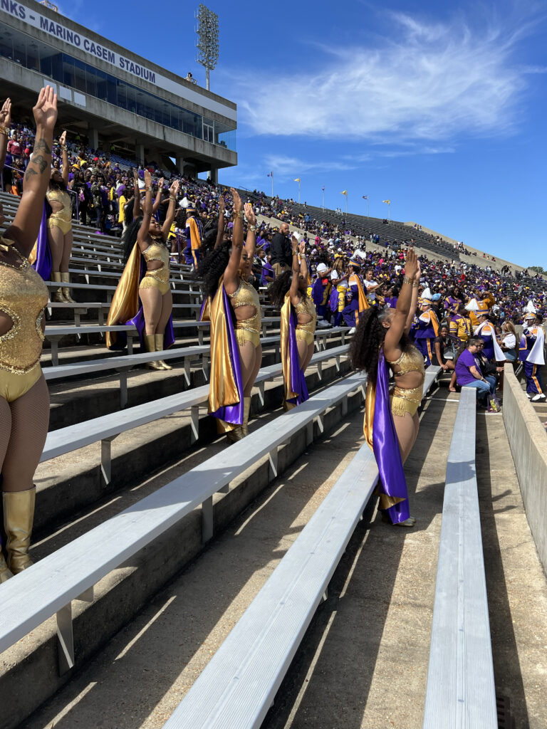 a group of dancers performing on the bleachers during a football game wearing gold and purple uniforms